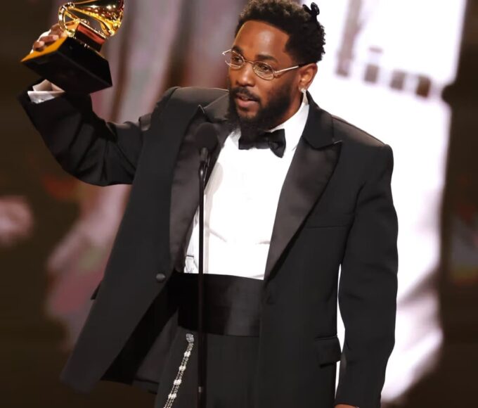Kendrick Lamar no palco do Grammy Awards 2026 segurando vários troféus após vencer cinco categorias, incluindo Música do Ano com “Luther”.