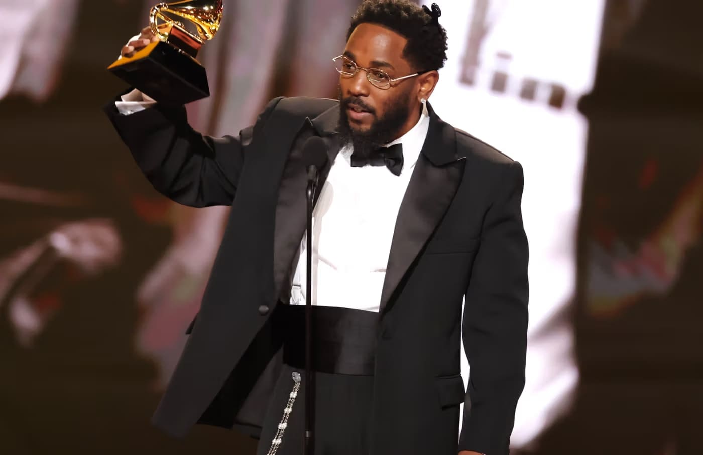 Kendrick Lamar no palco do Grammy Awards 2026 com troféus após vencer cinco categorias, incluindo Música do Ano com “Luther”.
